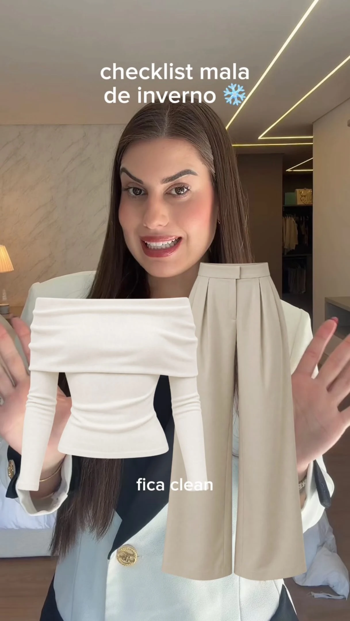 Raissa Dámian segurando uma blusa branca e um casaco bege em um conteúdo de mala de inverno